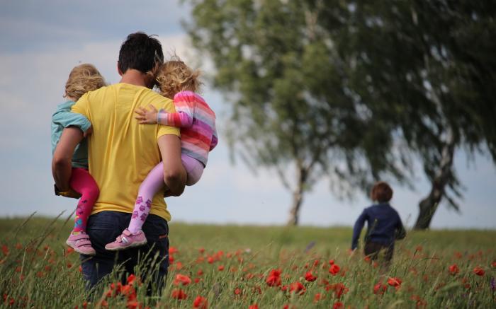 man carrying to girls on field of red petaled flower by Juliane Liebermann courtesy of Unsplash.